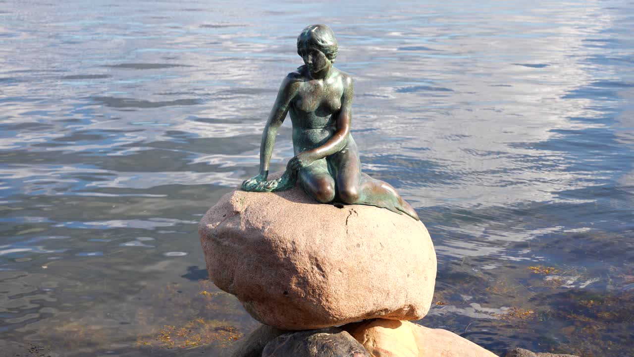 pequeña estatua de bronce de sirena en una roca junto a la orilla del agua en copenhague, dinamarca