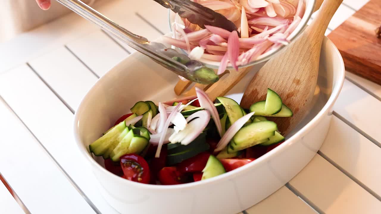 A vibrant salad with tomatoes, cucumbers, and shallots in a white bowl, captured in natural lighting