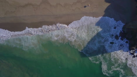 toma aérea descendente en cámara lenta de una impresionante playa con olas rompiendo
