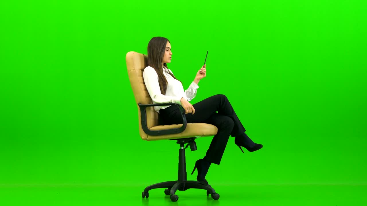 La bella donna sulla sedia da ufficio che parla su sfondo verde.
