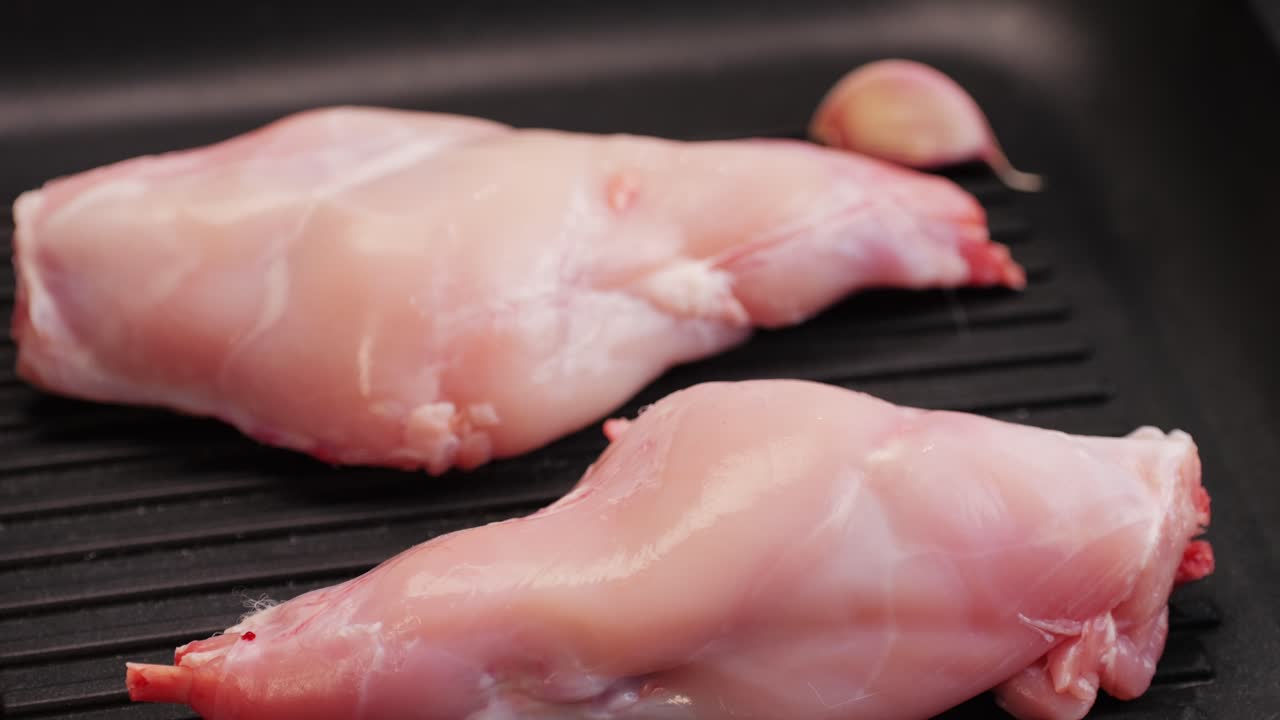 Roasted rabbit legs in a grill pan, healthy diet meat close up, chef cooking rabbit on kitchen restaurant, Black background. Top view