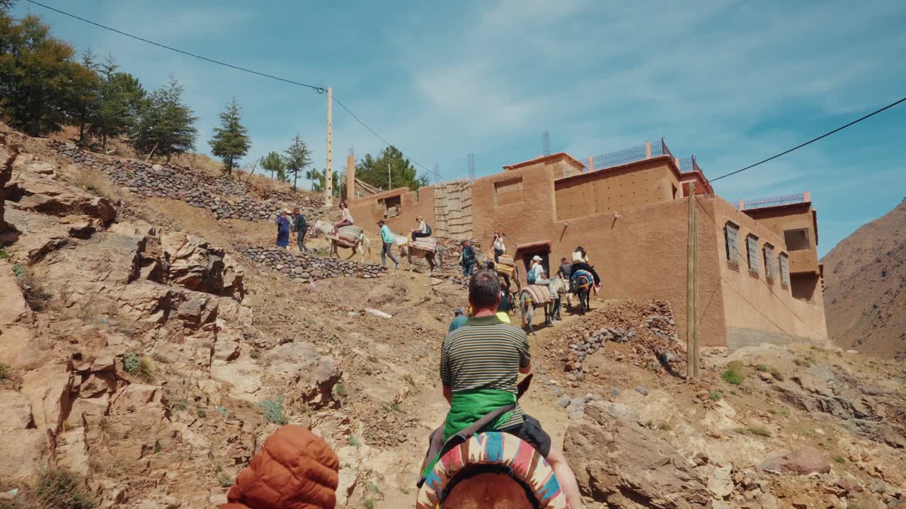 Wide shot of group of travelers riding mules to hike up at the Atlas Mountains in Morocco.