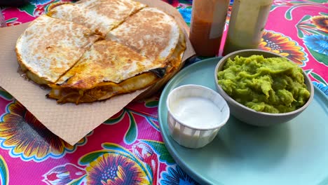 Deliciosa-Quasadilla-De-Pollo-Desmenuzado-Con-Guacamole,-Salsas-Picantes-Y-Crema-Agria-En-Un-Restaurante-Mexicano,-Tortilla-De-Pollo-Picante-Cocida-A-Fuego-Lento-Con-Queso,-Tiro-De-4k