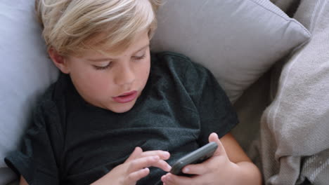 happy little boy using smartphone playing game relaxing on sofa at home child browsing online with mobile phone technology anti social addiction concept 4k footage