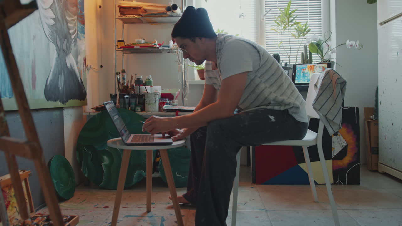 Artist Sitting in Creative Studio, Working on Laptop