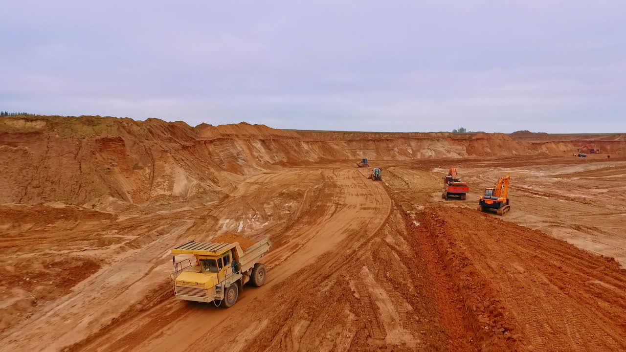 Dump truck driving through sand pit. Drone view. Crawler excavator extract sand