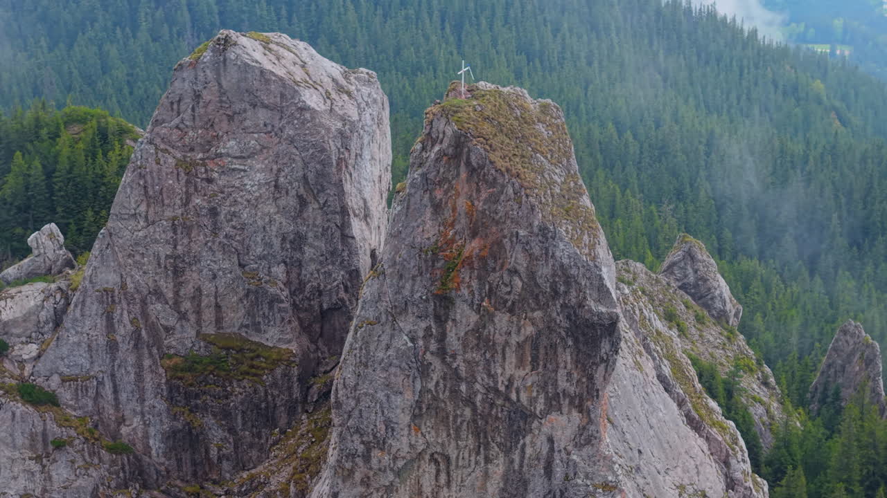 Rocky peaks of Pietrele Doamnei with a metal cross on top, surrounded by coniferous forests in Rarau Mountains, Romania
