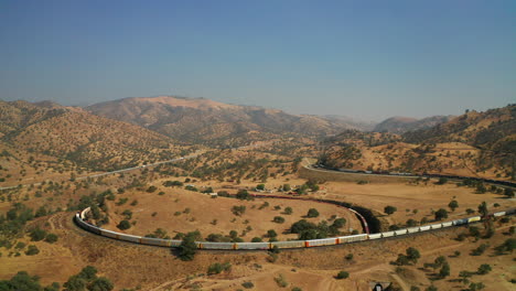 as one train sits idle on the tracks another train climbs the tehachapi loop - aerial view