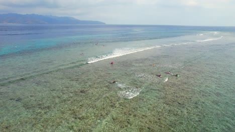 surfistas surfeando en marea baja en las islas gili tratando de atrapar pequeñas olas en el océano índico, aéreo