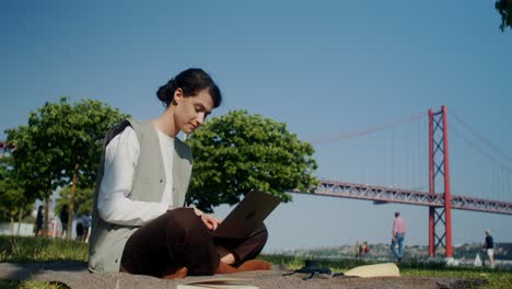 woman working on laptop in park by the bridge