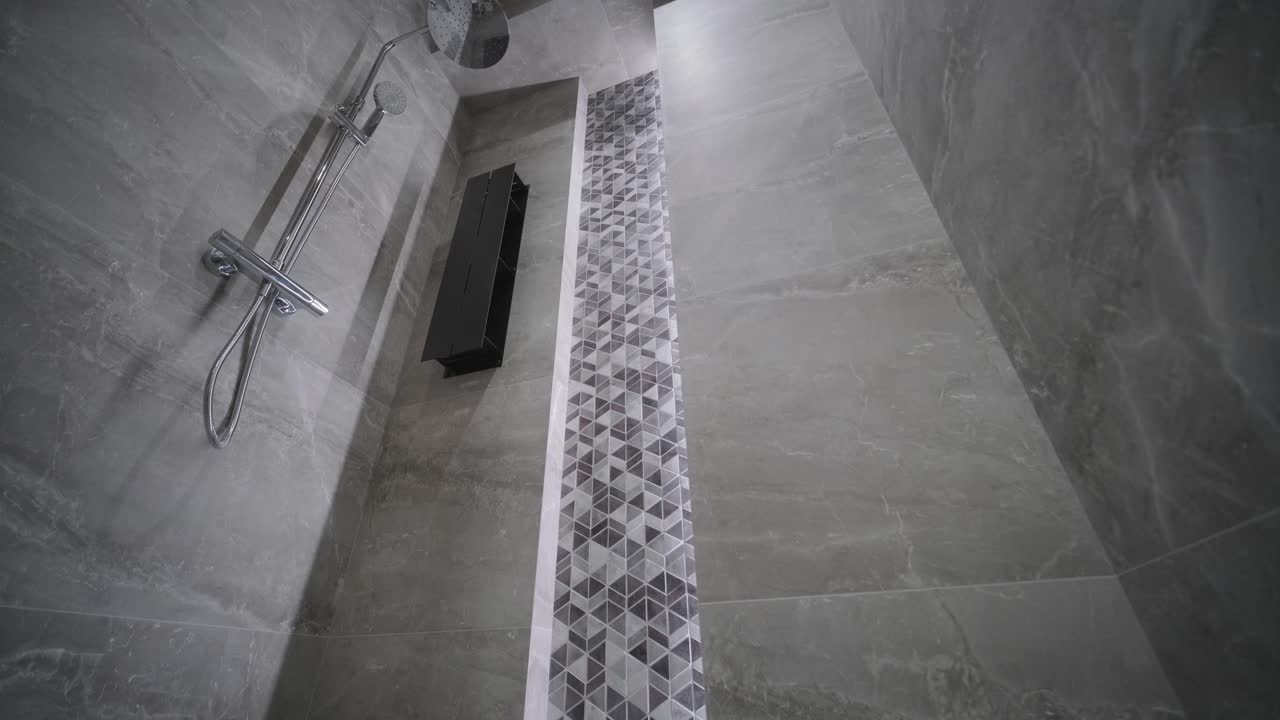 baño moderno con una ducha minimalista con una franja de azulejos de patrón geométrico y accesorios elegantes, colocados contra paredes de piedra gris