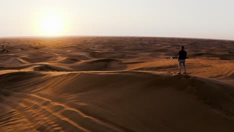 Hombre-Parado-En-El-Desierto-Al-Atardecer-A-La-Izquierda-En-Movimiento-Tiro-Aéreo-De-Drones