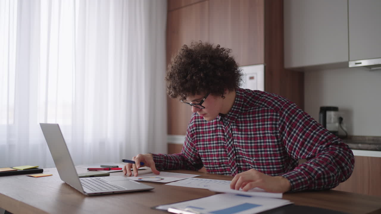 A man with glasses at the table shows a picture with graphs in the camera of the laptop