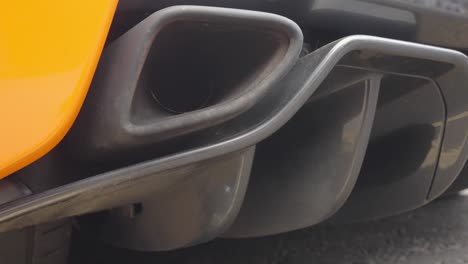 Closeup-footage-of-large-black-exhaust-tail-pipe-on-a-yellow-sports-car