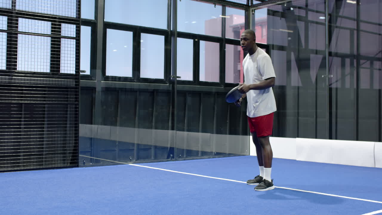 Man playing padel tennis on indoor court, hitting ball with focus and agility