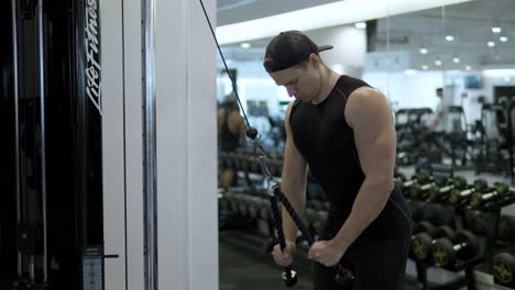 Focused-male-athlete-pulling-down-rope-on-cable-machine,-pumping-up-triceps-muscles