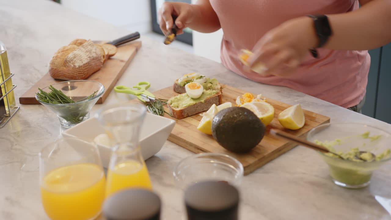 Preparing healthy breakfast, woman spreading avocado on toast with boiled eggs