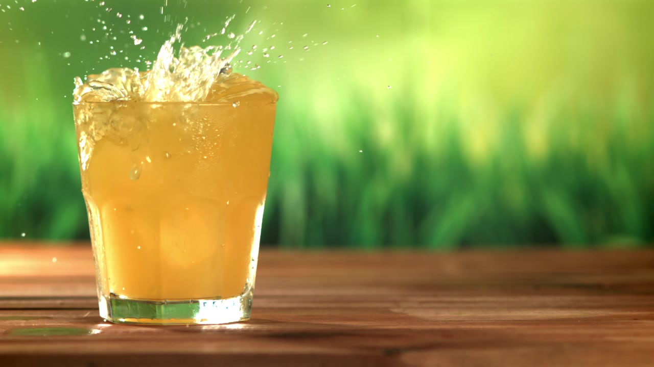 Ice Cube Splashing into a Glass of Refreshing Juice in Slow Motion