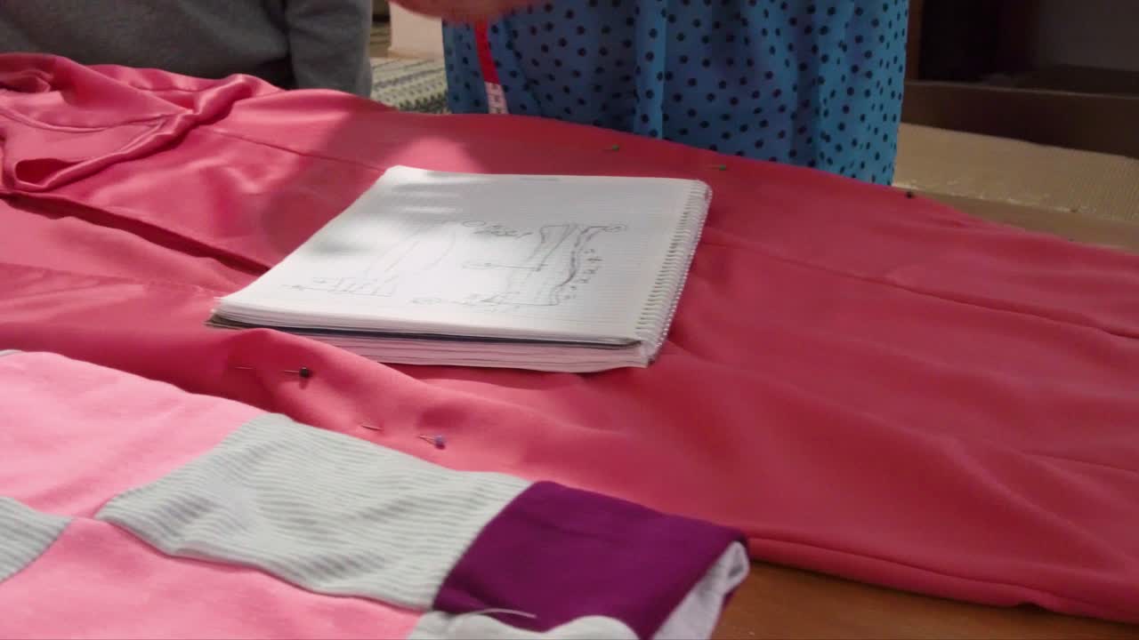 diseñador de moda latino tomando medidas de un vestido en una mesa de madera usando un cuaderno