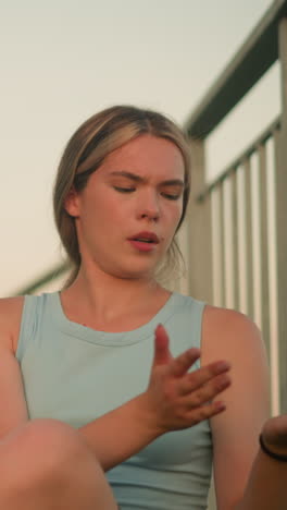 joven sentada cerca de la barandilla de hierro limpiando la suciedad de la palma, respirando profundamente con los ojos cerrados, la luz del sol de la noche iluminando suavemente la cara, con una camiseta azul claro, con un brazalete de mano negro