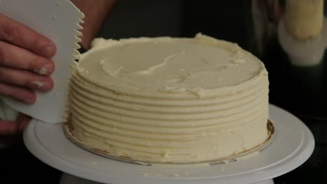 A-baker-uses-a-tool-to-shape-the-sides-of-a-frosted-cake