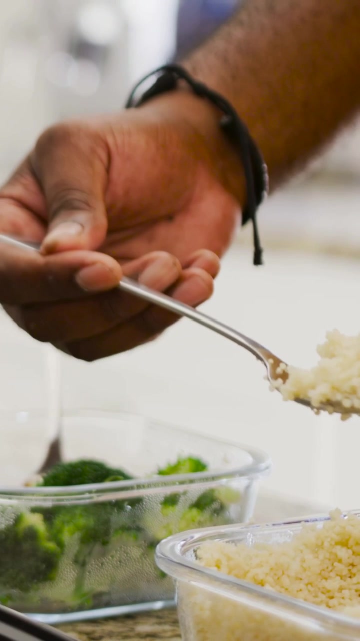 Video verticale: Mano che si allunga per raccogliere il riso e confezionare un pasto in una scatola nera per la preparazione sul bancone, broccoli