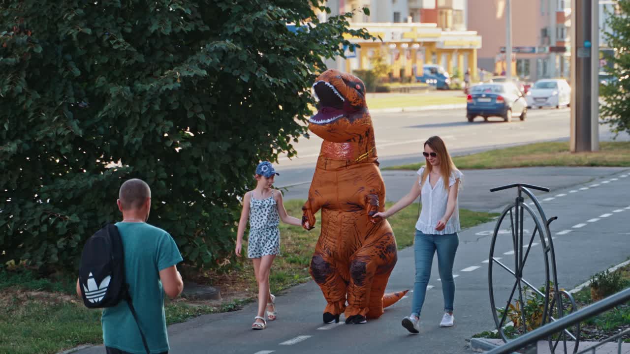 Dinosaur costume at city sidewalk. Family walks with big dinosaur in city