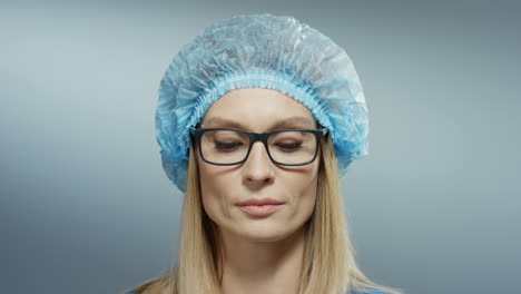 Primer-Plano-De-La-Joven-Doctora-Rubia-De-Buen-Aspecto-Con-Cara-Seria-En-Sombrero-Azul-Y-Gafas-Mirando-A-La-Cámara