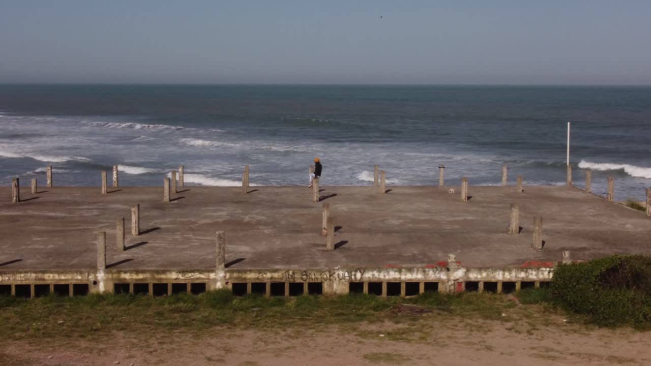 Aerial orbiting view around the person sitting on abandoned building front to the ocean, Chapadmalal-Buenos Aires in Argentina natural background