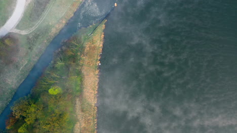 Toma-Aérea-De-Arriba-Hacia-Abajo-De-La-Orilla-De-Un-Río,-Por-Encima-De-Las-Nubes-De-Niebla-De-La-Madrugada