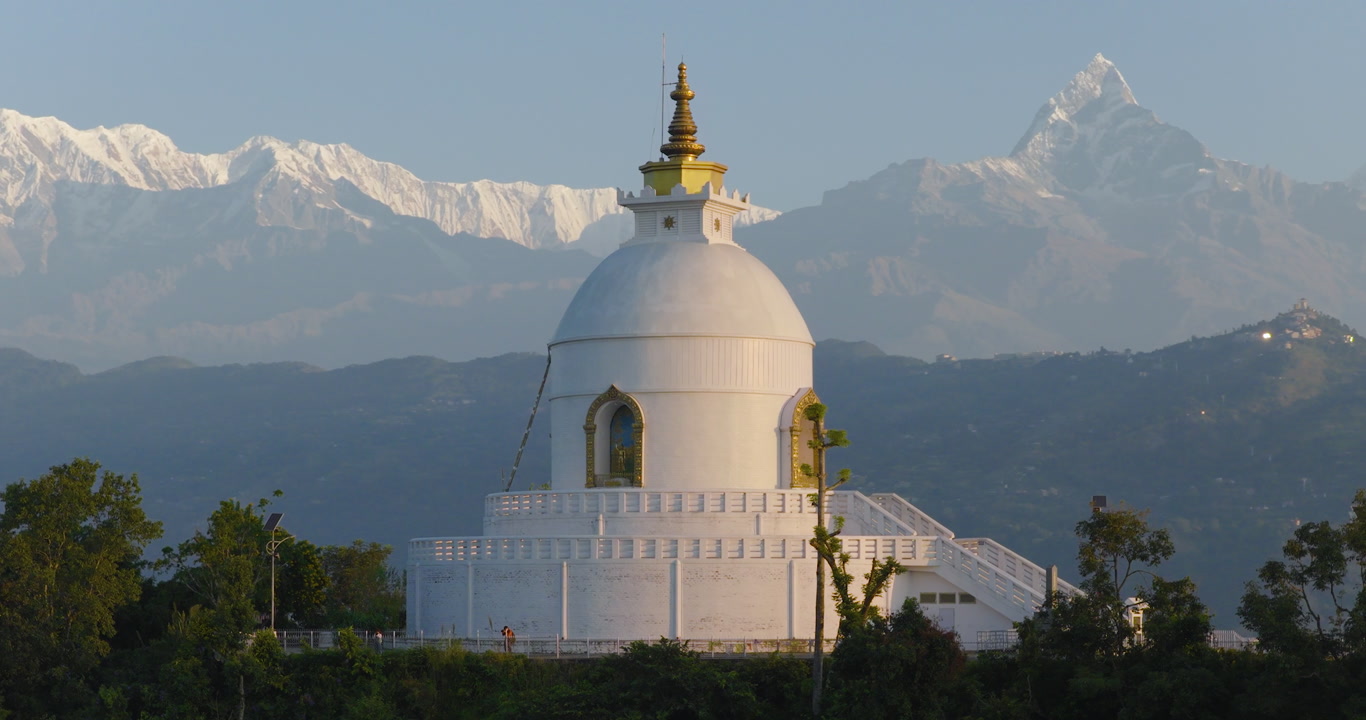 Aerial orbit of Buddhist monument World Peace Stupa in Pokhara Nepal with snow-capped Annapurna and Machhapuchhre peaks passes in the background.