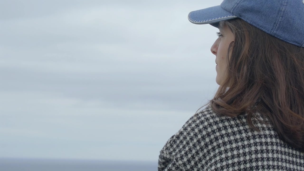 Woman in denim cap gazing at the distant ocean horizon