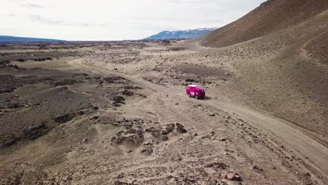 aerial of a rare pink land rover 101 driving through the outback highlands of desolate iceland