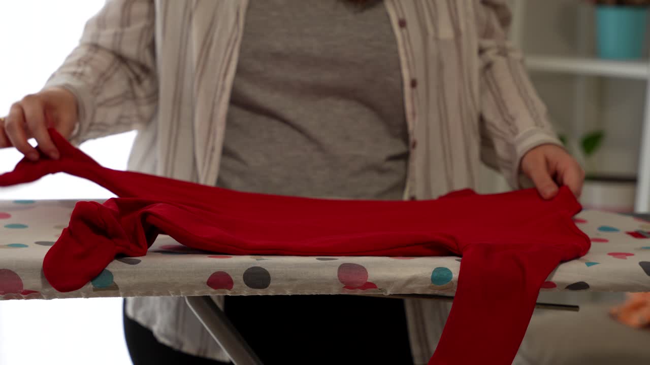Pregnant woman ironing a red pyjamas for her future baby. Close up