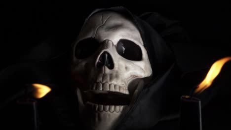 Hooded-skull-open-mouthed-with-two-candles-on-dark-background