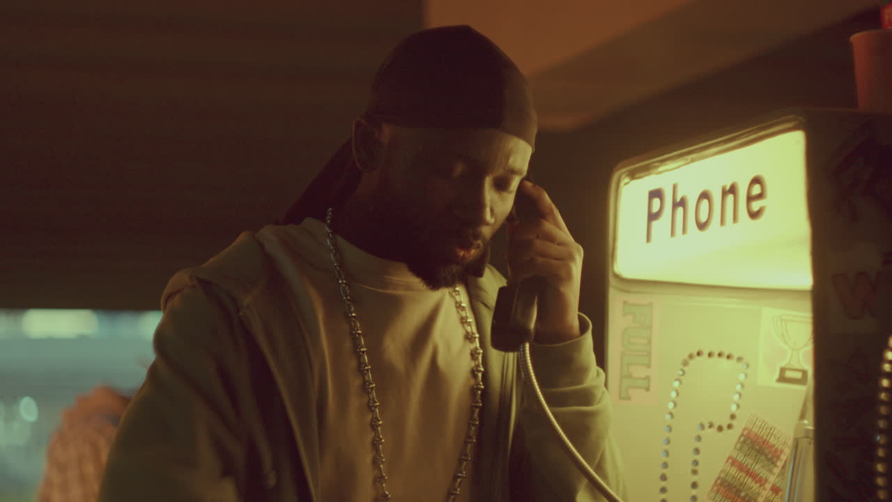 hombre negro teniendo una conversación emocional en el teléfono público de la calle por la noche