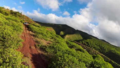 Vista-Aérea-De-Un-Camino-Que-Atraviesa-La-Vegetación-Baja,-Frente-A-Un-Cielo-Azul-Claro-Con-El-Imponente-Pico-De-La-Montaña-Molokai-Al-Fondo