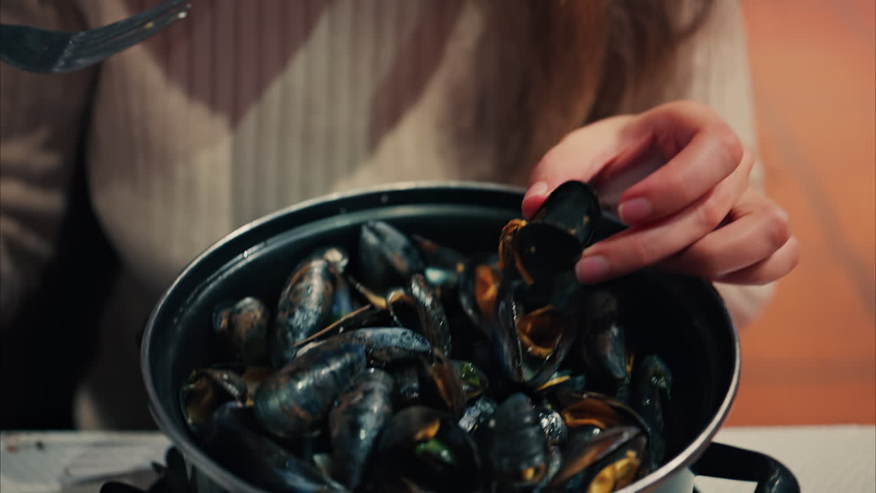 Close up of a woman eating mussels from a pan with a fork
