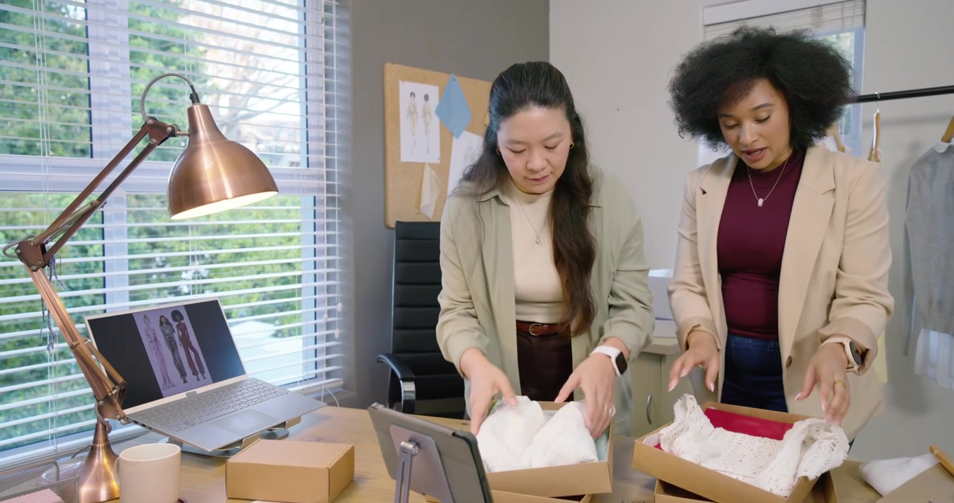 Colleghe che aprono nuove scatole, smistano capi d'abbigliamento in studio, controllano il laptop e imballano gli ordini
