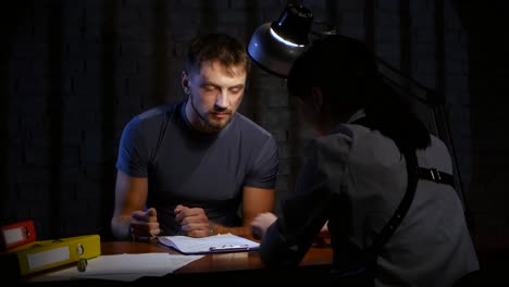 woman detective is the interrogation a dangerous criminal man woman detective is the interrogation a dangerous criminal man in handcuffs they sit at the table where stacked folders with documents and evidence glow lamp suspect surrenders of irrefutable clue