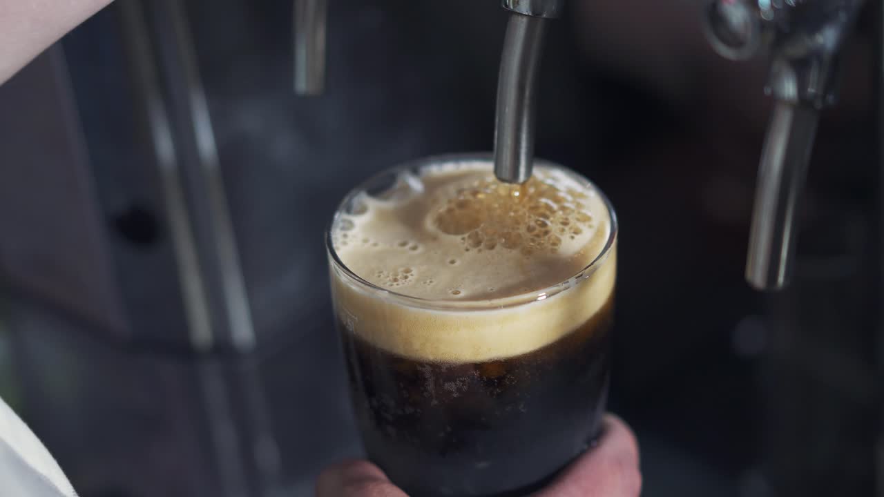 Close up of barman's hand pouring beer from the beer tap into the glass in the pub. Process of pouring beer with foam