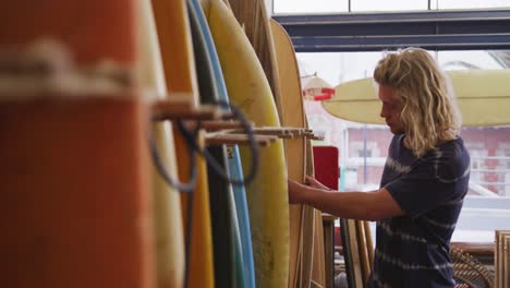 Kaukasischer-Männlicher-Surfbrettbauer,-Der-Eines-Der-Surfbretter-In-Seinem-Studio-überprüft