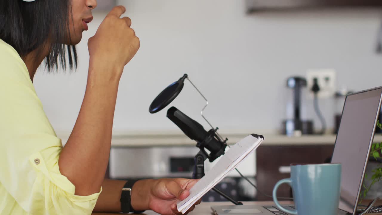 persona de raza mixta de género fluido grabando un podcast usando una computadora portátil leyendo notas en casa