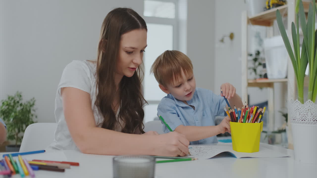una familia de dos niños y una joven madre sentada en la mesa dibuja en papel con lápices de colores. desarrollo de la creatividad en los niños. interior blanco limpio