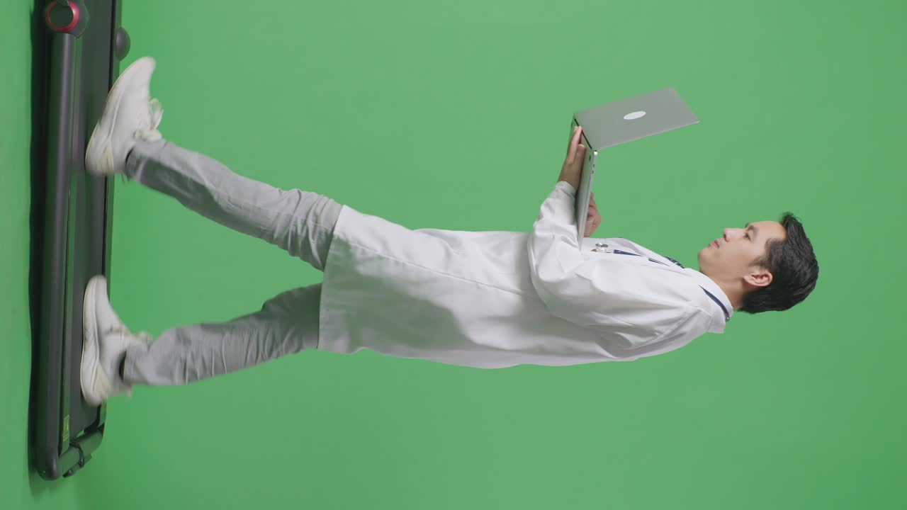 아시안 남성 의사가 스테토스코프를 들고 노트북을 사용하면서 병원에서 녹색 화면 배경에서 고 있습니다.