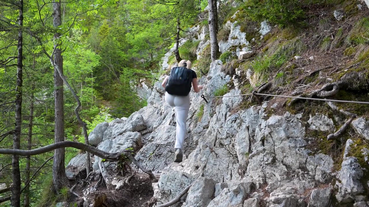 Blonde caucasian woman walking on challenging mountain path leading to Soca River spring in Slovenia, wide shot, static