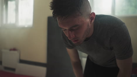 tired male athlete with sweat on face breathes deeply resting after long boxing session in basement of gym. exhaustion and fatigue after exercise