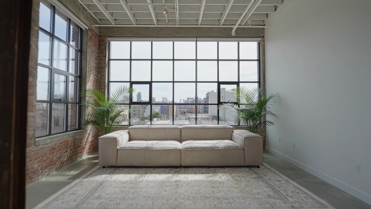 Panning camera moving closer from wide view toward beige three seat sofa in loft, revealing skyline