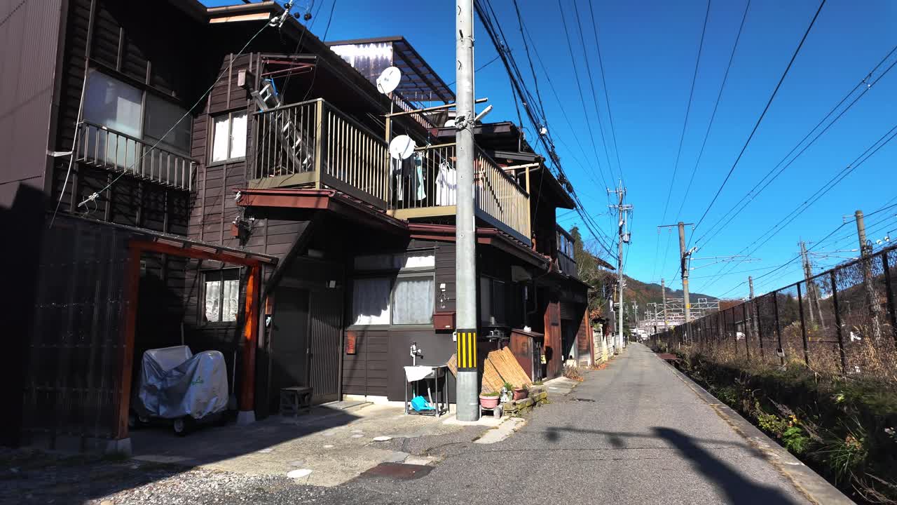 Quiet residential street with traditional wooden houses and overhead power lines in Narai juku, Japan, on a clear, sunny day