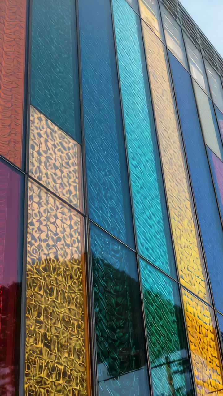 Vertical video: Tilting camera revealing tall colored glass facade outside, showing sky and frames